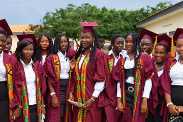 Group of high school aged girls standing in graduation caps and gowns with their diplomas