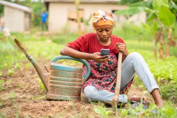 Woman sitting on the ground with farming tools on smart phone 