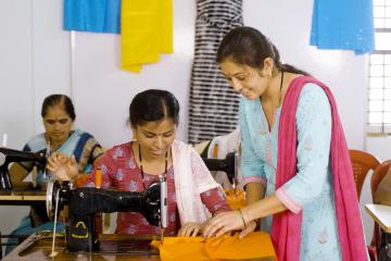 Woman working at a sewing machine with an instructor standing next to her helping
