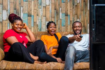 Two women and a man watch television while smiling