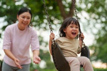 Mother pushing young daughter on swingset
