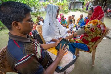 A man on the left checks a woman's vitals on the right while they both sit down.