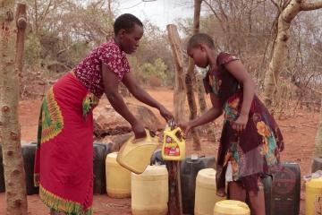 Mother and child filling water jugs at a tap