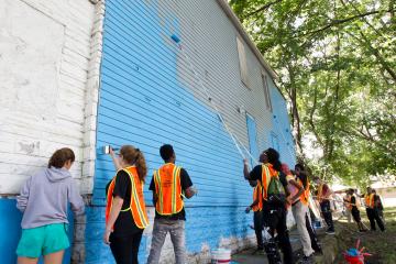 Youth in safety vests painting a wall