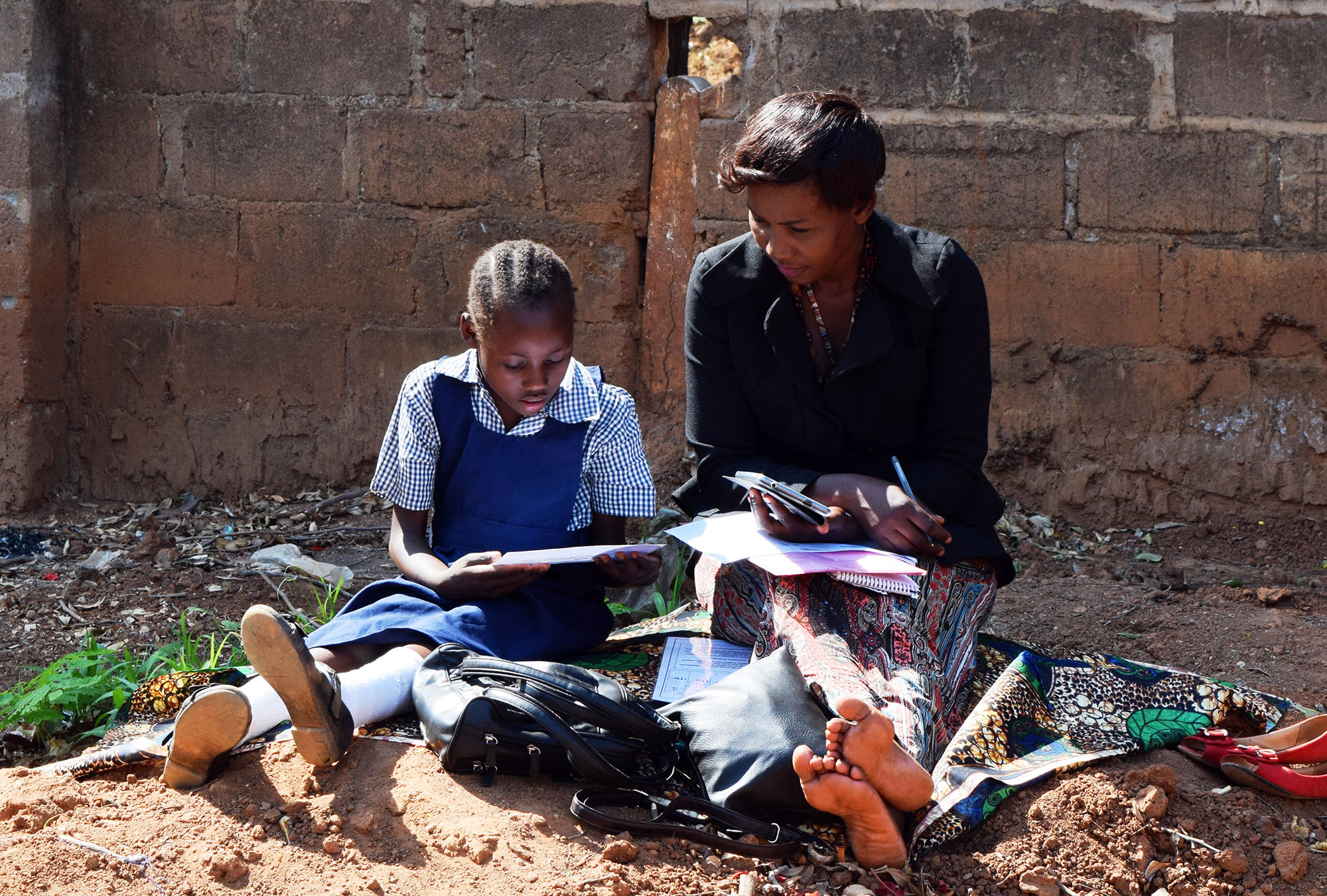 Woman sits reading a book with a child in school uniform